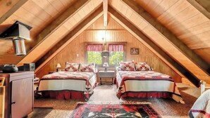 A cozy attic bedroom with two beds, a wooden ceiling, and a window with curtains.