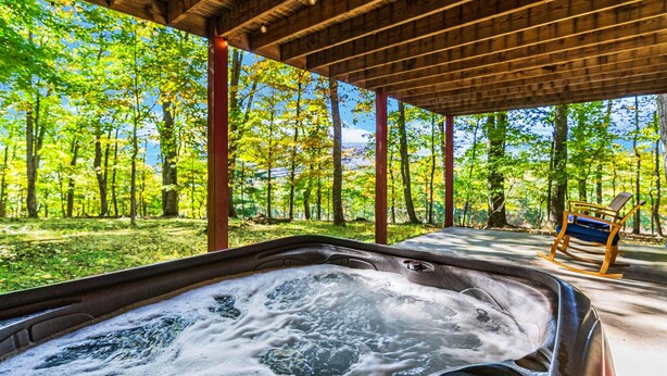 Un jacuzzi con cubierta de madera y una mecedora, rodeado de zona boscosa.