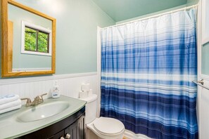 A bathroom with a green sink, a mirror, a toilet, and a blue striped shower curtain. - Cozy woodland cabin w/ hot tub & deck (Berkeley Springs)