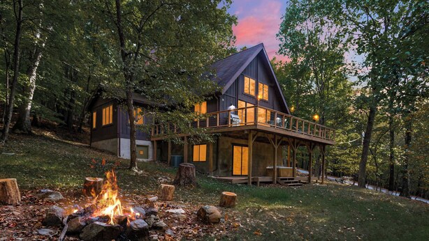 A cabin with a deck, a fire pit, and a view of the surrounding forest. - Cozy woodland cabin w/ hot tub & deck (Berkeley Springs)