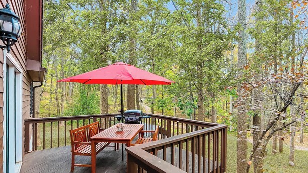 Un terrazzo in legno con tavolo e sedie, un barbecue e un ombrellone rosso.