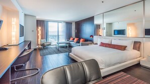 A modern hotel room with a large bed, a desk, a chair, and a sofa.