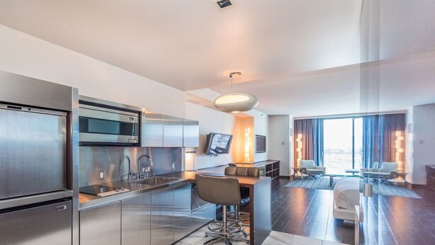 A modern hotel room with a kitchen area, a dining table, and a seating area with a view.