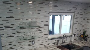 A modern kitchen with a granite countertop, stainless steel appliances, and a backsplash with a brick pattern. - Bright & Airy St. Pete Home w/ Outdoor Living (St. Petersburg)