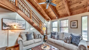 A spacious living room with a high ceiling, wooden beams, two sofas, a coffee table, and a staircase.