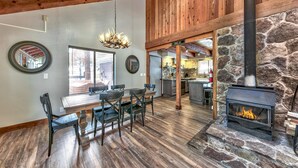 A spacious dining area with a wooden table and chairs, a stone fireplace, and a kitchen in the background.