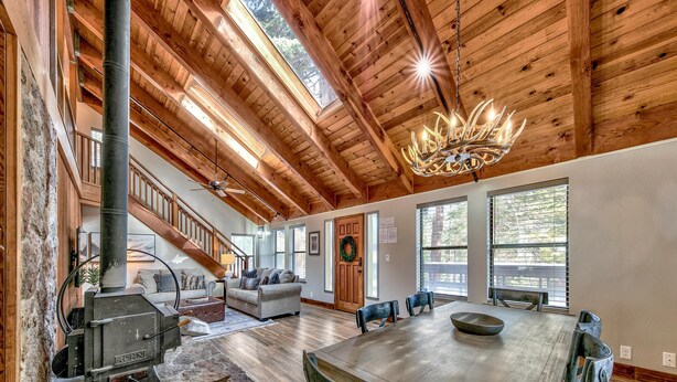 A spacious living area with a high ceiling, wooden beams, a fireplace, a dining table, and a staircase leading to an upper level.
