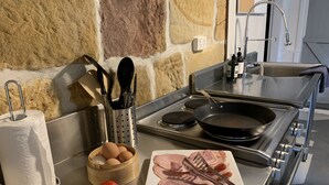 A kitchen with a stone wall, a stainless steel sink, a stove, and a countertop with eggs, tomatoes, and ham. - Historic Georgian Stone Built Cottage (Saint Albans)