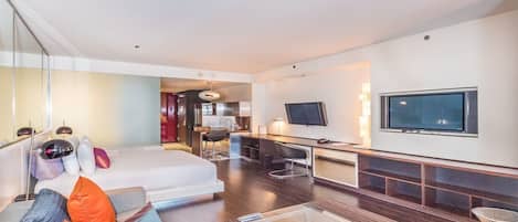 Una habitación de hotel moderna con una cama grande, un sofá, una mesa de centro de vidrio, un televisor y una zona de escritorio.