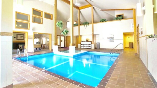 Una piscina interior con suelo de baldosas, vigas de madera y una zona de recepción con mostrador y plantas.