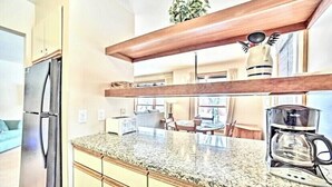 Una cocina con encimera de granito, cafetera y refrigerador.