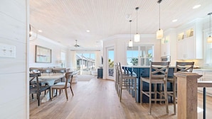 Una cocina amplia con suelo de madera, armarios blancos e iluminación colgante.