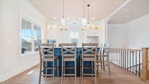 Una cocina moderna con armarios blancos, una isla azul y sillas de madera.