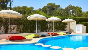 A swimming pool with multiple lounge chairs and umbrellas, surrounded by greenery. - Canyamel Garden Apartments (Capdepera)