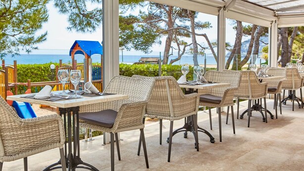 An outdoor dining area with wicker chairs and tables, overlooking a beach and the sea. - Canyamel Garden Apartments (Capdepera)