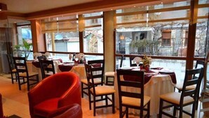 Ein Restaurant mit Tischen, Stühlen, großen Fenstern und Blick auf die Straße.