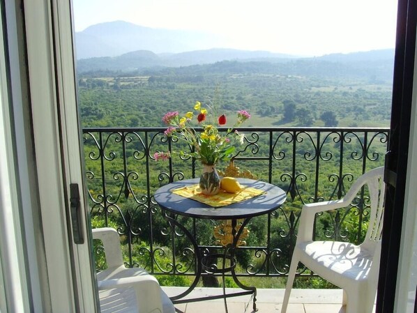 A balcony with a table, chairs, and a vase of flowers.