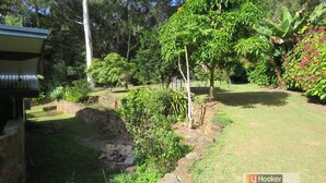Un jardin avec un mur en pierre, différentes plantes et un bâtiment doté d’un toit en pente.