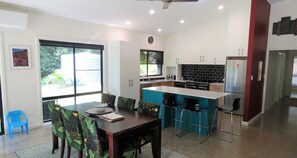 A modern kitchen with a dining area, featuring a large window, a built-in island, and a refrigerator. - THE GLEN - 3 BEDROOM RAINFOREST RETREAT (Arakoon)