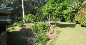 A garden with a stone wall, various plants, and a building with a sloped roof. - THE GLEN - 3 BEDROOM RAINFOREST RETREAT (Arakoon)