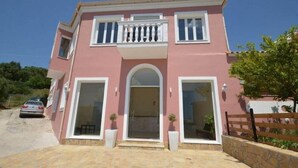 A two-story house with a pink facade, large windows, and a balcony. - Paradiso Apartments (Corfu)
