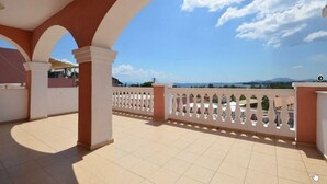 A covered outdoor area with a tiled floor, white railings, and a view of distant mountains under a clear sky. - Paradiso Apartments (Corfu)