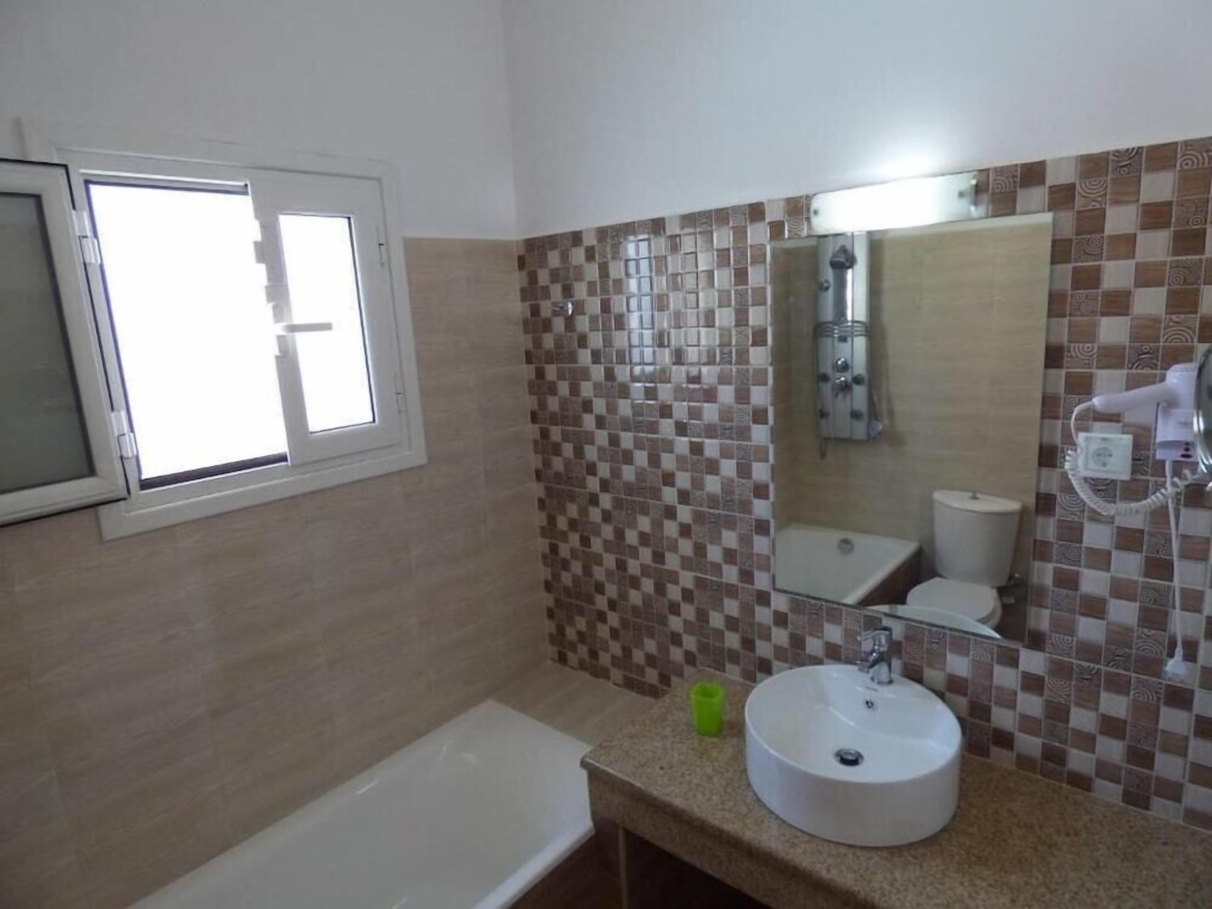 Un bagno con parete piastrellata, lavandino, specchio, finestra e wc.