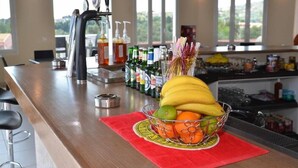 A kitchen counter with a fruit bowl containing bananas, oranges, and limes, and a variety of bottles and a coffee machine. - Paradiso Apartments (Corfu)