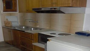 Cuina amb armaris de fusta, un rentaplat de coure inoxidable, forn encastrat i nevera blanca.