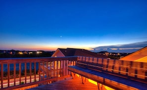 Um deck de madeira com guarda-corpo, com vista para um corpo d'água e edifícios ao longe.