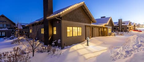A snow-covered residential area with houses featuring large windows and a chimney.