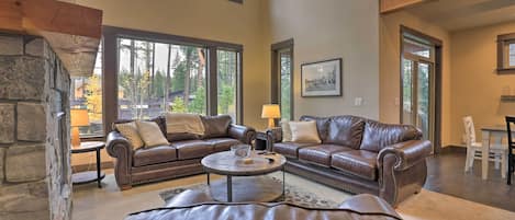 A spacious living room with a stone fireplace, leather sofas, and large windows offering a view of the outdoors.