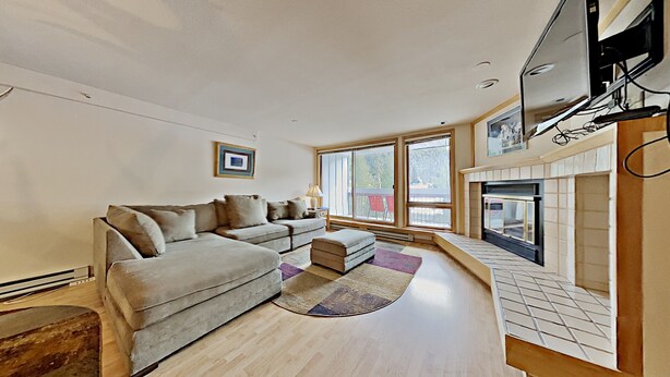 A living room with a sofa, ottoman, fireplace, and large windows. - Liftside 205 (Keystone)