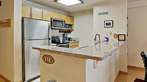 A compact kitchen with a central island, built-in microwave, and stainless steel appliances. - Liftside 205 (Keystone)