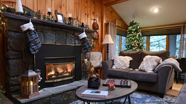 A cozy living room with a stone fireplace, a Christmas tree, and a comfortable couch. - Schroon River Retreat, Waterfront, Near Lake George & Gore Mountain, Hot tub (Warrensburg)