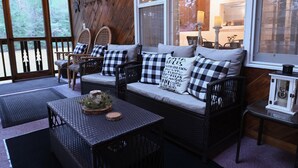 A cozy cabin interior with a sofa set, wicker chairs, a table with a centerpiece, and a lantern. - Schroon River Retreat, Waterfront, Near Lake George & Gore Mountain, Hot tub (Warrensburg)