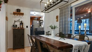 A dining area with a long wooden table, chairs, a white vase with greenery, and a sign that reads "gathers wine o'clock". - Schroon River Retreat, Waterfront, Near Lake George & Gore Mountain, Hot tub (Warrensburg)