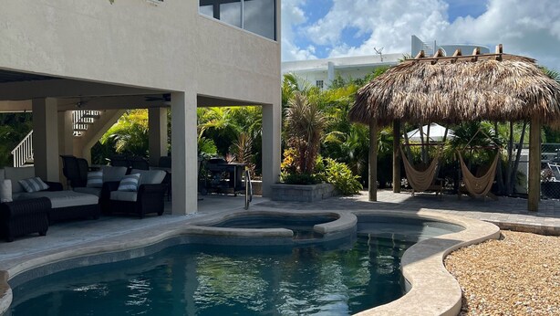 A modern pool area with a curved design, outdoor seating, and a thatched-roof structure.