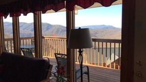 Una stanza con vista sulle montagne, un terrazza in legno, un tavolo con sedie e una lampada.