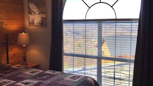 Una camera da letto con una grande finestra, un letto con una coperta a motivi decorativi, una lampada e un'opera d'arte appesa al muro.