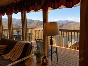 A cozy room with a view of a lake and mountains, featuring a wooden deck, a sofa, and a table with a lamp. - Gatlinburg, Autumn Leaves, Great Mountain Views, Hot Tub, Pool Table, Fireplace. (Gatlinburg)