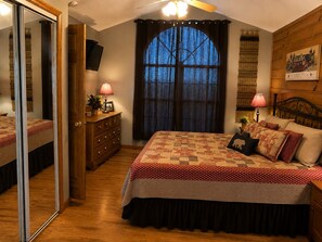 A bedroom with a large bed, a dresser, a mirror, a window with curtains, and a ceiling fan. - Gatlinburg, Autumn Leaves, Great Mountain Views, Hot Tub, Pool Table, Fireplace. (Gatlinburg)