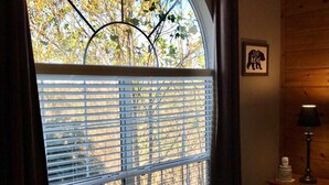 Una camera da letto con un'ampia finestra ad arco, un letto con copripiumino decorato, un comodino con una lampada e un quadro incorniciato appeso al muro.