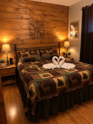 A bedroom with a wooden headboard, a patterned bedspread, two bedside lamps, and a decorative wall piece. - Gatlinburg, Autumn Leaves, Great Mountain Views, Hot Tub, Pool Table, Fireplace. (Gatlinburg)