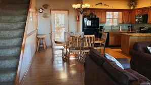 Un'ampia zona giorno con scala in legno, un tavolo da pranzo con sedie, un divano e una cucina con mobili in legno e frigorifero.
