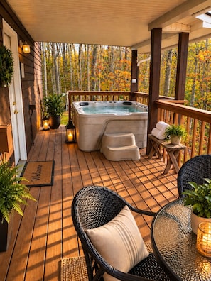 Une terrasse en bois avec un jacuzzi, des fauteuils en osier, une table en verre et un paillasson.