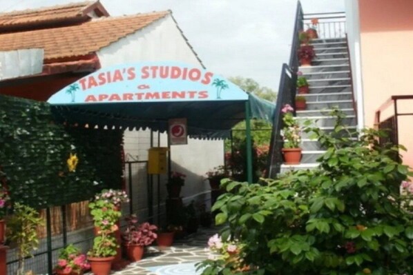 Une enseigne indiquant « TASIA’S STUDIOS & APARTMENTS », avec une entrée abritée et des plantes en pot disposées autour.