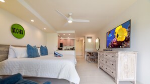 A bedroom with a bed, a TV, a ceiling fan, and a kitchen in the background. - Lahaina Shores Beach Resort Studio (Lahaina)