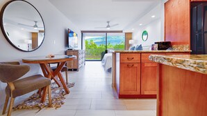 A modern kitchen with wooden cabinets, a granite countertop, and a dining area with a round table and chairs. - Lahaina Shores Beach Resort Studio (Lahaina)