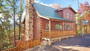Une cabane en rondins avec une cheminée en pierre, une véranda avec une balustrade et une vue sur la forêt environnante.